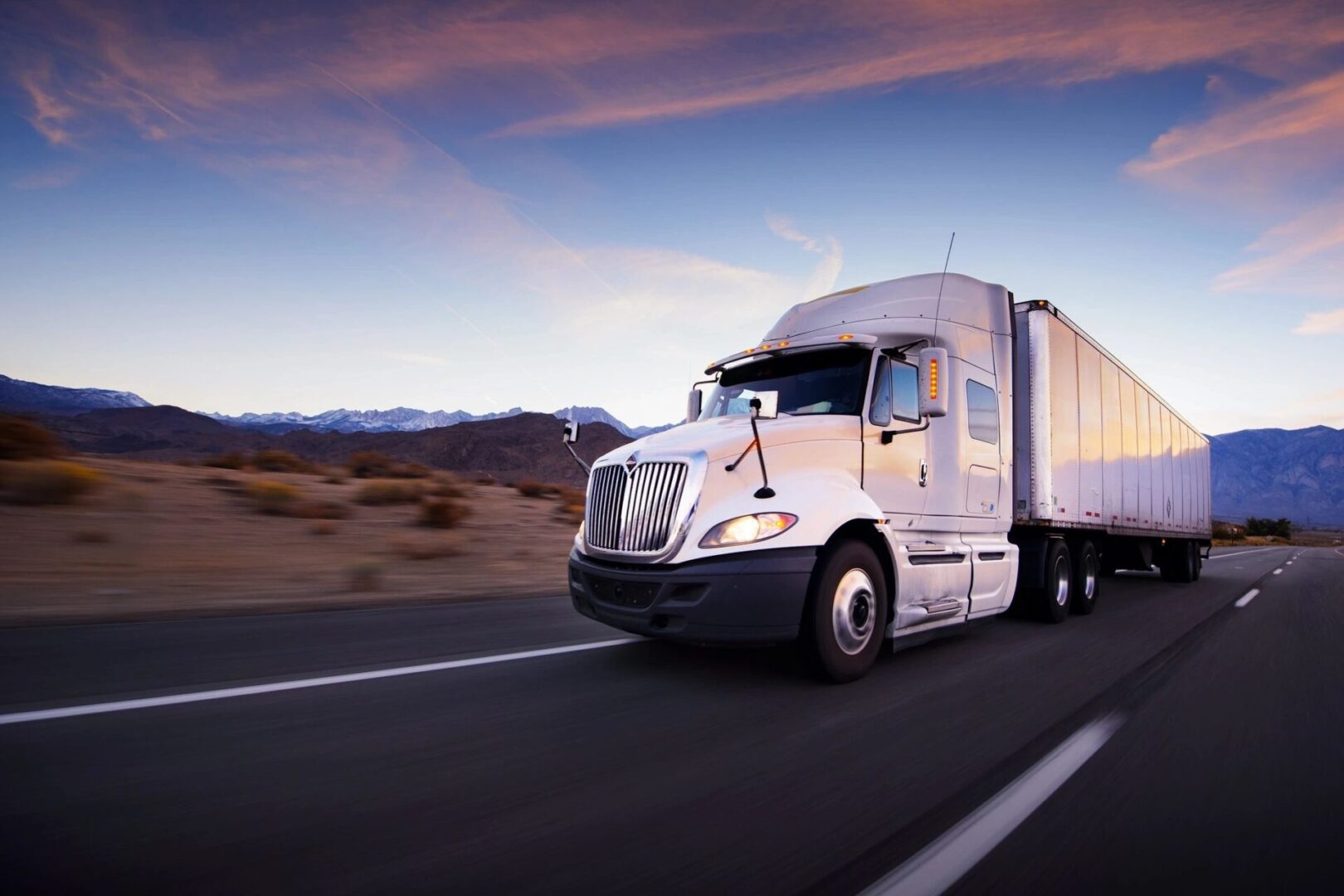 Truck driving on highway at sunset.