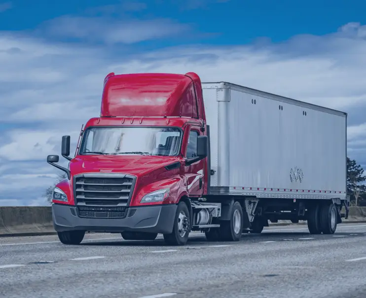 A red semi-truck parked on a road under a blue sky.