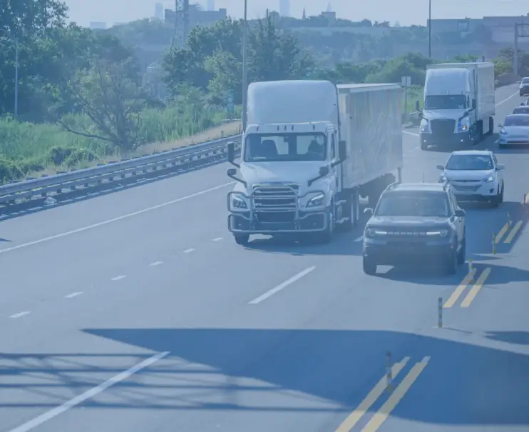 Semi-trucks and cars traveling on a highway surrounded by greenery.