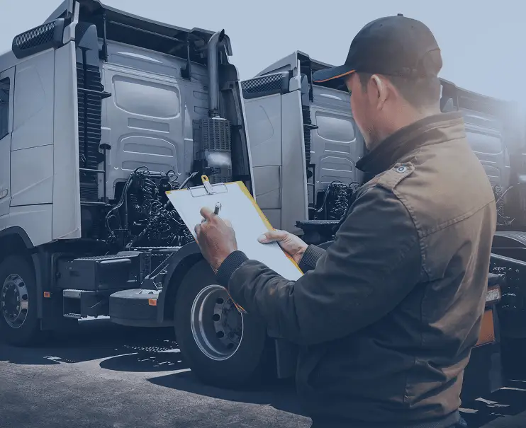 Technician inspecting a truck and taking notes on a clipboard.