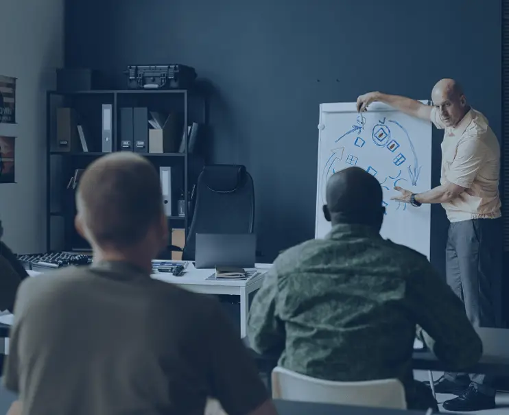 A man explains a strategy on a whiteboard to two seated colleagues in an office.