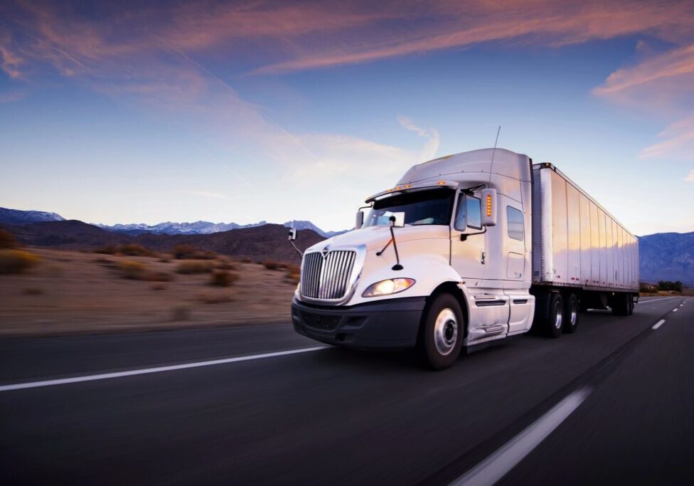 Truck driving on highway at sunset.